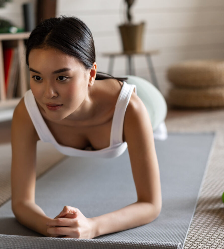 Sporty asian girl in activewear doing workout at home, follow video sport guide, online fitness instructor on laptop, standing in plank on floor mat.